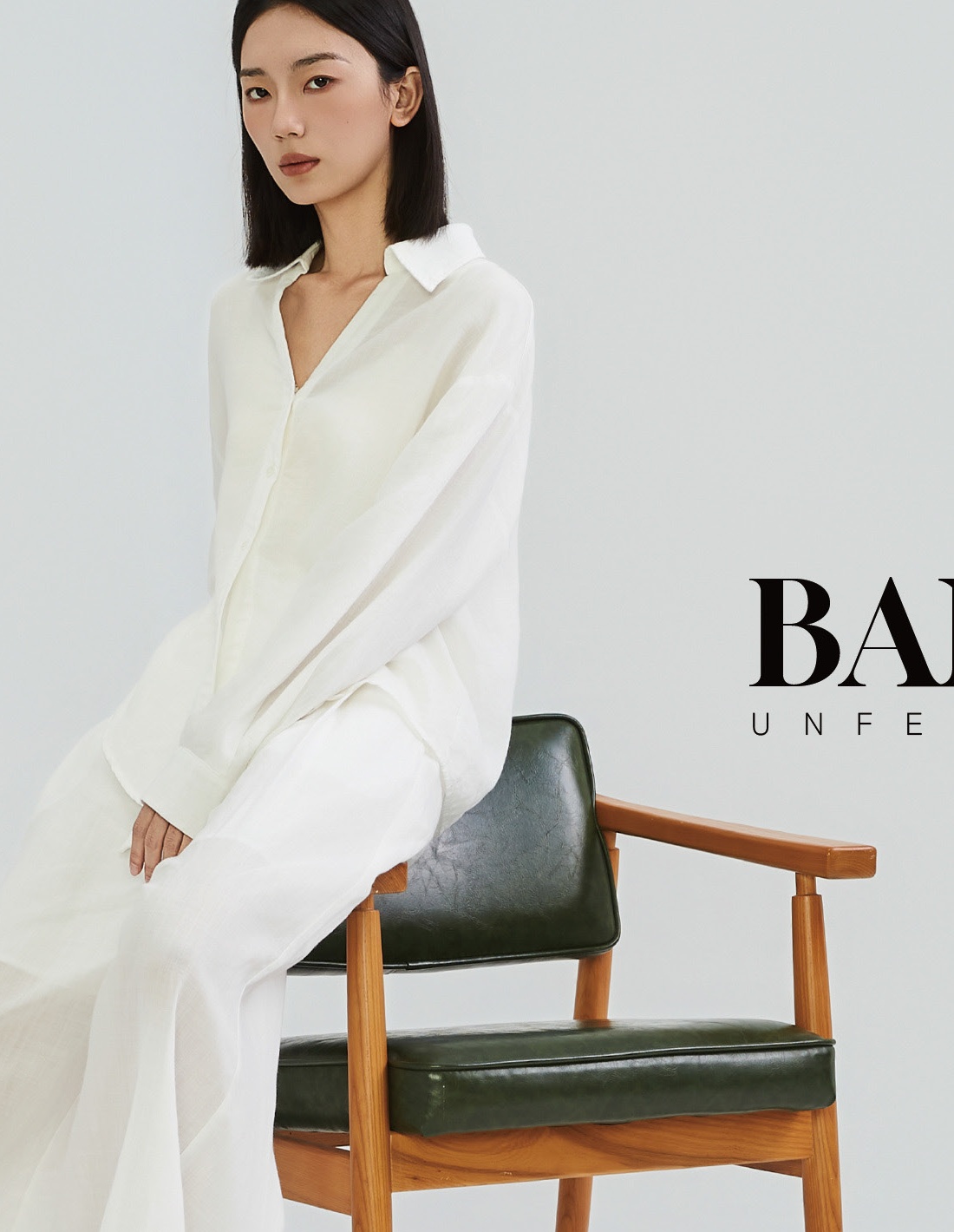 她屿女装 HERISLET 2026 夏季主形象 — 白色衬衫长裙与墨绿皮椅，静奢风松弛通勤风格